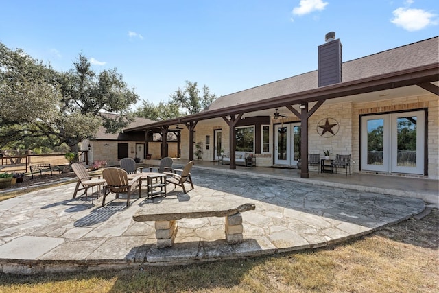 rear view of property with french doors, a patio area, ceiling fan, stone siding, and a fire pit