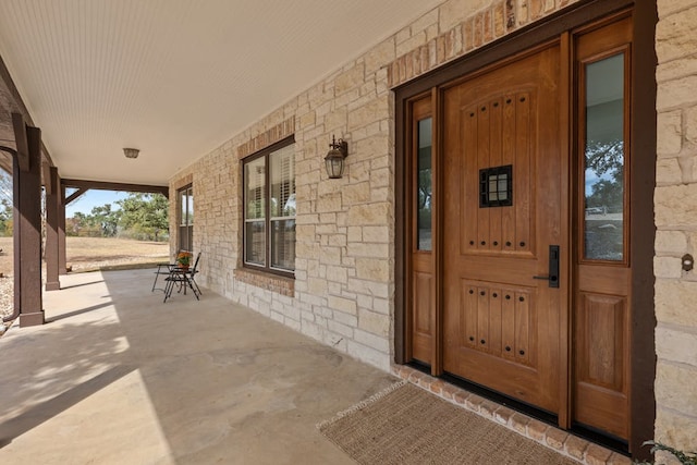 view of exterior entry featuring covered porch and stone siding