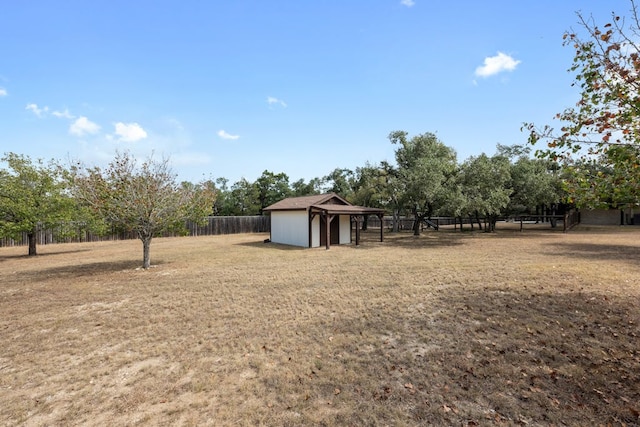 view of yard featuring a rural view, an outdoor structure, a shed, and fence