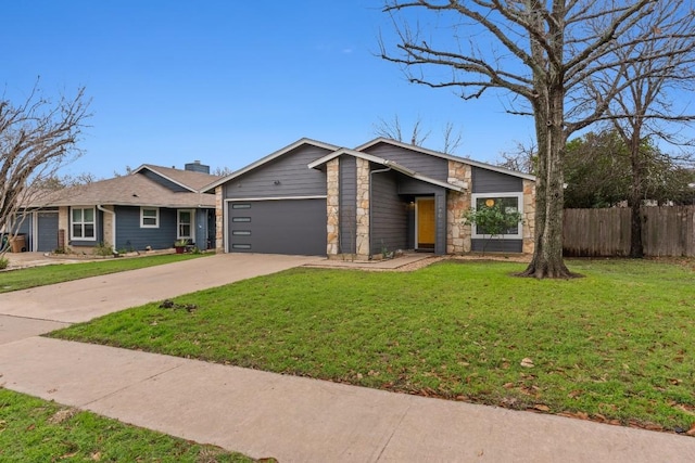 view of front of property with an attached garage, stone siding, a front yard, and fence