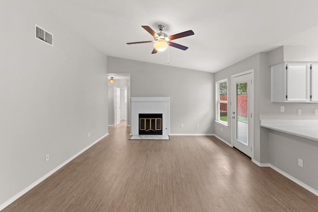 unfurnished living room featuring wood finished floors, a fireplace with flush hearth, baseboards, visible vents, and a ceiling fan