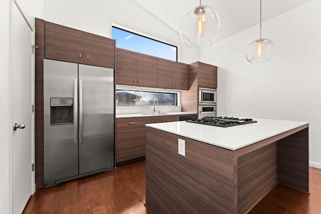 kitchen featuring dark wood finished floors, appliances with stainless steel finishes, light countertops, pendant lighting, and a sink