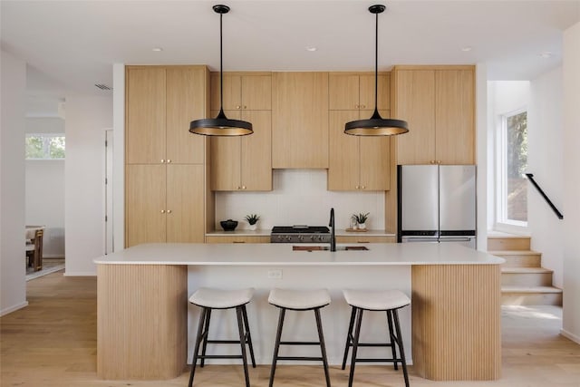 kitchen featuring light brown cabinets, freestanding refrigerator, and a sink