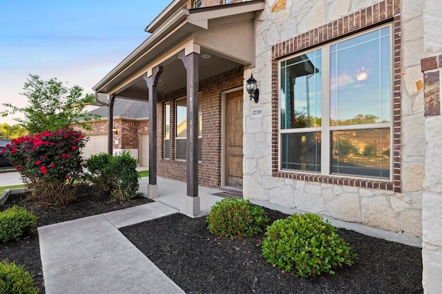 entrance to property featuring covered porch, stone siding, brick siding, and an attached garage