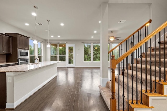 kitchen featuring stainless steel appliances, dark wood-style flooring, visible vents, dark brown cabinets, and light stone countertops