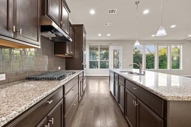 kitchen with a center island with sink, visible vents, decorative light fixtures, under cabinet range hood, and a sink