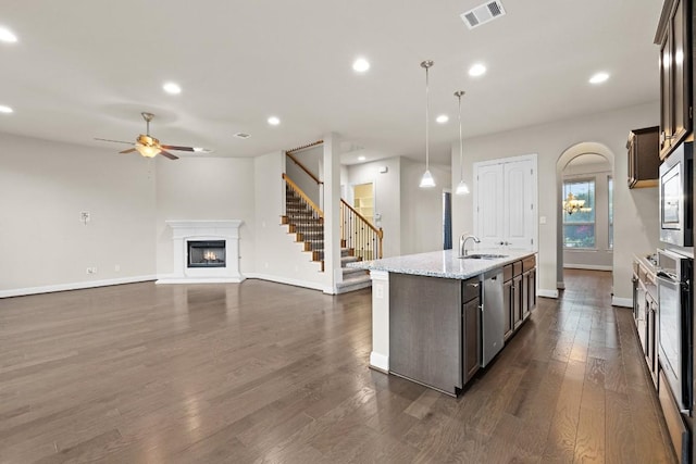 kitchen featuring visible vents, dark brown cabinetry, decorative light fixtures, and a center island with sink