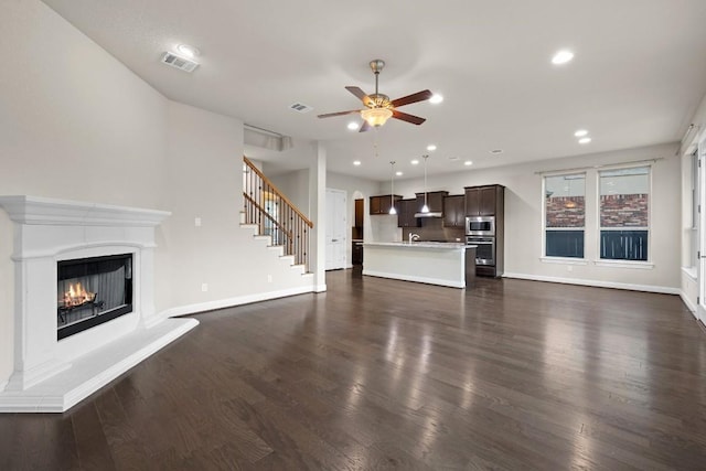 unfurnished living room featuring baseboards, a lit fireplace, stairway, and dark wood-style flooring