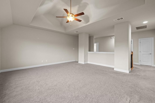 empty room with a raised ceiling, visible vents, a ceiling fan, light carpet, and baseboards