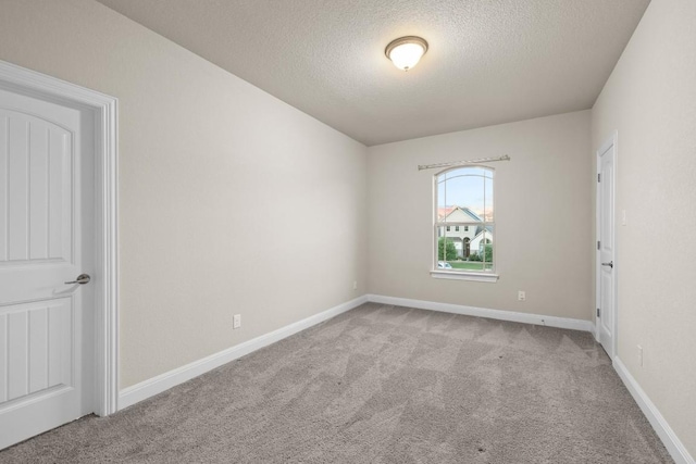 spare room with light carpet, a textured ceiling, and baseboards