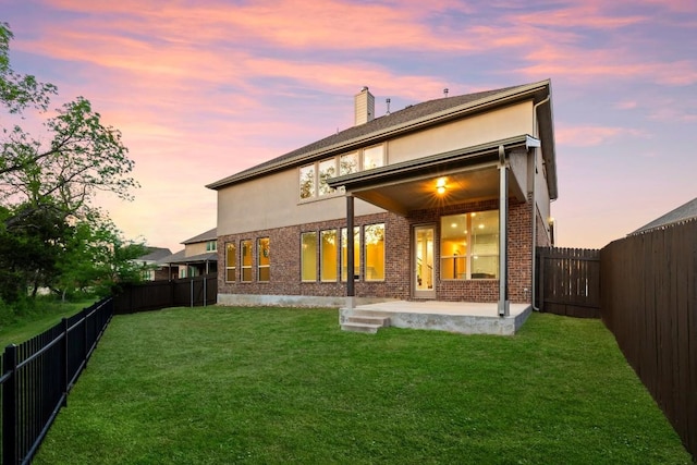 back of property with a yard, a patio area, brick siding, and a fenced backyard