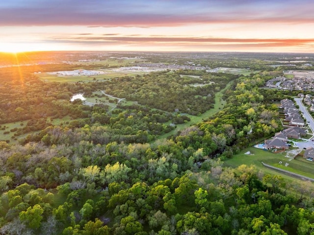 aerial view at dusk featuring a wooded view