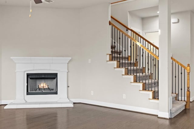 unfurnished living room with a warm lit fireplace, visible vents, baseboards, ceiling fan, and dark wood-type flooring