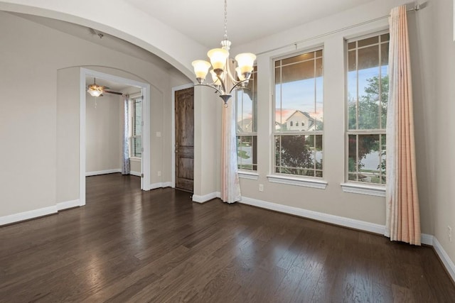 unfurnished dining area featuring baseboards, arched walkways, dark wood-style flooring, and ceiling fan with notable chandelier