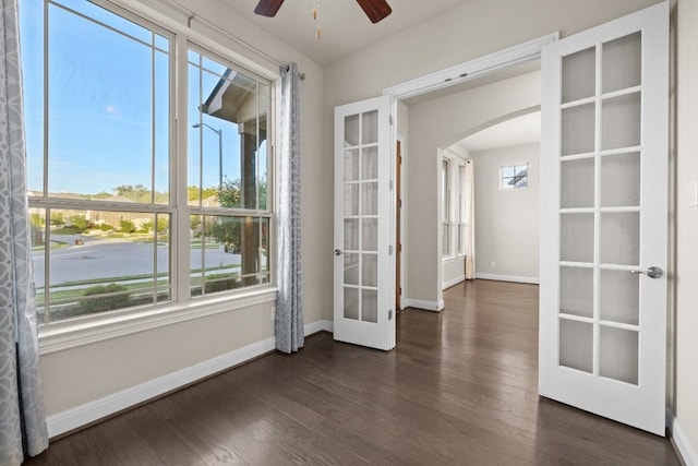 unfurnished room with arched walkways, french doors, dark wood finished floors, and a healthy amount of sunlight