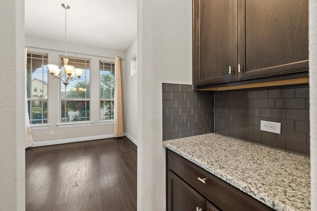 kitchen with dark wood-style floors, pendant lighting, tasteful backsplash, dark brown cabinets, and light stone countertops