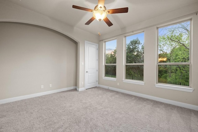 empty room featuring light carpet, baseboards, arched walkways, and a ceiling fan