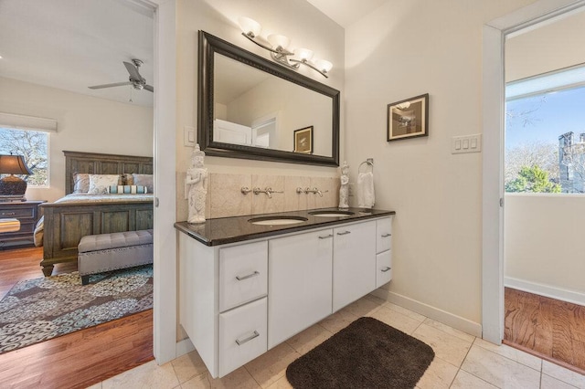 ensuite bathroom featuring connected bathroom, a ceiling fan, tile patterned floors, double vanity, and tasteful backsplash