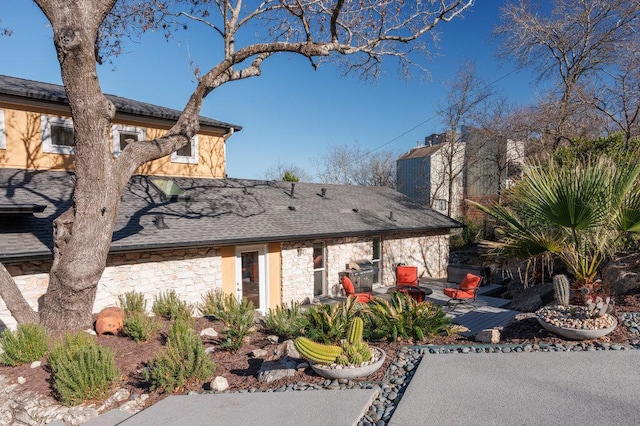 exterior space with stone siding, roof with shingles, a patio, and a chimney