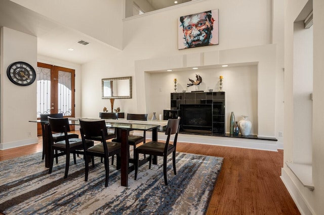 dining space with dark wood-type flooring, a high ceiling, visible vents, french doors, and a tiled fireplace