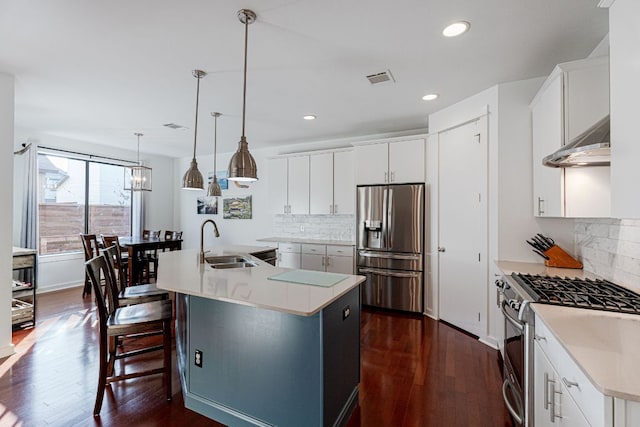 kitchen with hanging light fixtures, appliances with stainless steel finishes, a kitchen island with sink, and white cabinetry