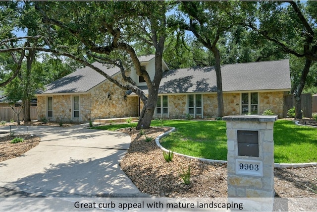 ranch-style home featuring concrete driveway, roof with shingles, a front yard, and fence