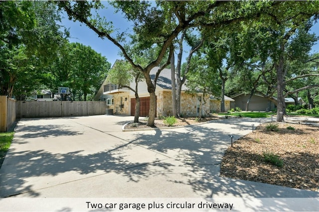 view of front of house featuring driveway, stone siding, and fence