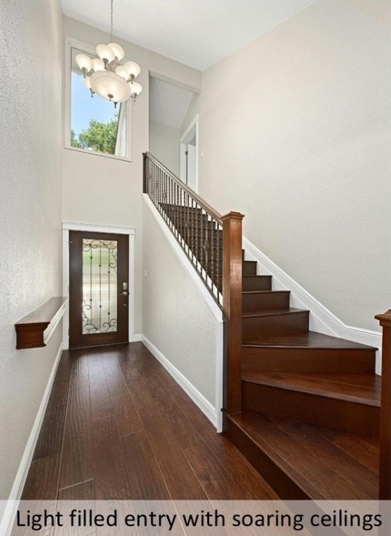 entryway with stairs, dark wood-style flooring, a chandelier, and baseboards