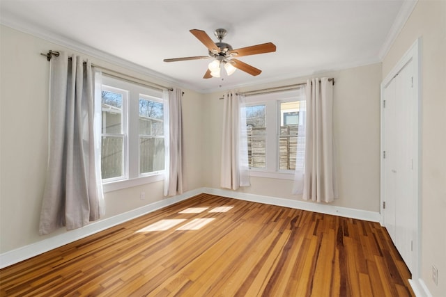 unfurnished room with baseboards, plenty of natural light, wood finished floors, and crown molding