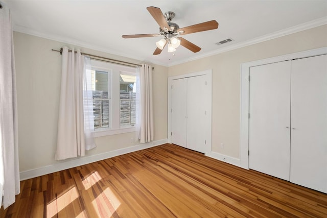 unfurnished bedroom featuring visible vents, baseboards, light wood-style floors, ornamental molding, and two closets