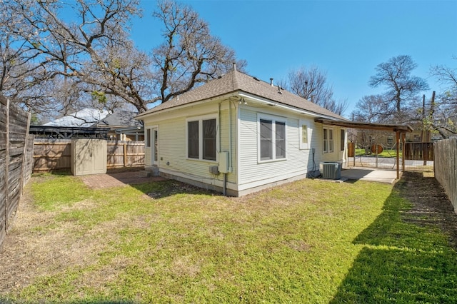 rear view of house with cooling unit, a fenced backyard, and a yard