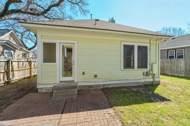 rear view of house featuring entry steps, roof with shingles, fence, and a lawn