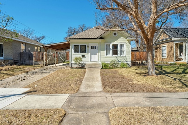 bungalow with concrete driveway, an attached carport, roof with shingles, and fence