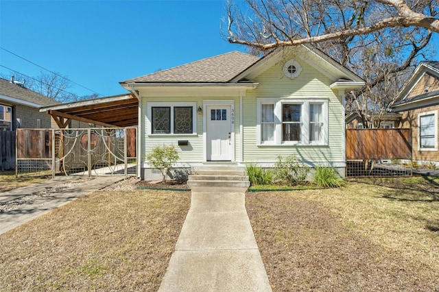 bungalow-style house with roof with shingles, concrete driveway, fence, an attached carport, and a front lawn