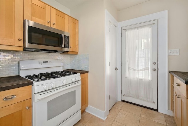 kitchen featuring light tile patterned floors, white range with gas cooktop, tasteful backsplash, dark countertops, and stainless steel microwave