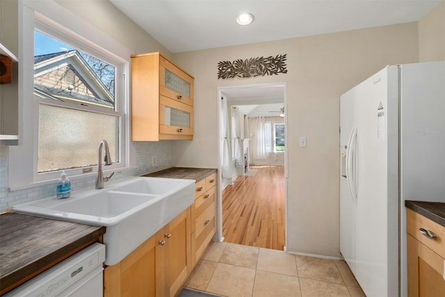 kitchen featuring light tile patterned floors, white appliances, a sink, tasteful backsplash, and dark countertops