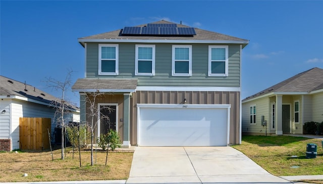 view of front of house with solar panels, an attached garage, board and batten siding, a front yard, and fence