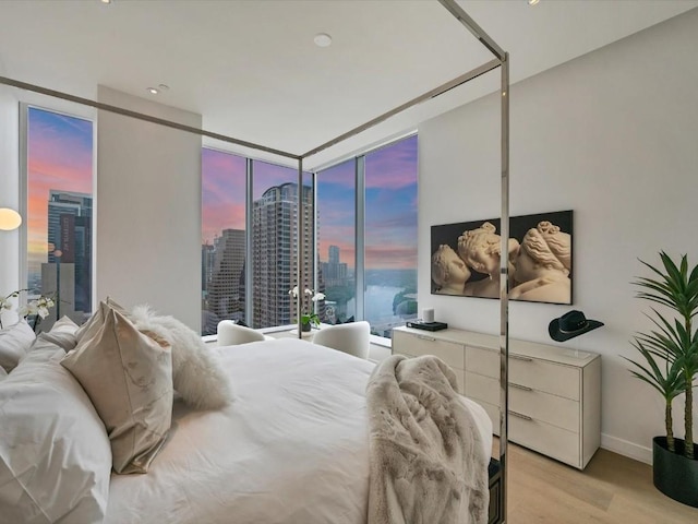 bedroom with baseboards, floor to ceiling windows, light wood-style floors, and a city view