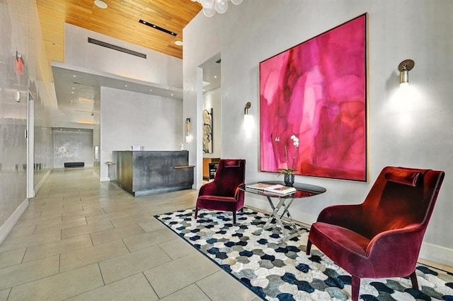 living area featuring wooden ceiling, tile patterned flooring, visible vents, a towering ceiling, and baseboards