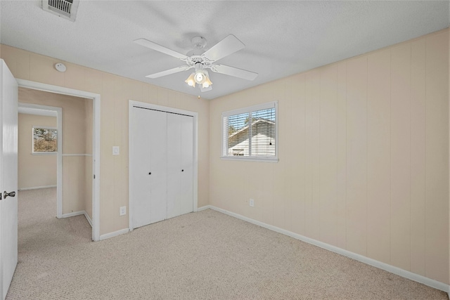 unfurnished bedroom featuring light carpet, a textured ceiling, visible vents, and a closet