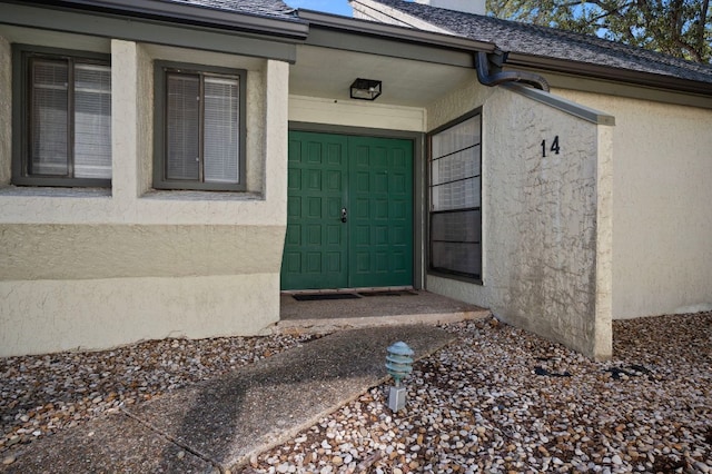 doorway to property with an attached garage, a shingled roof, and stucco siding