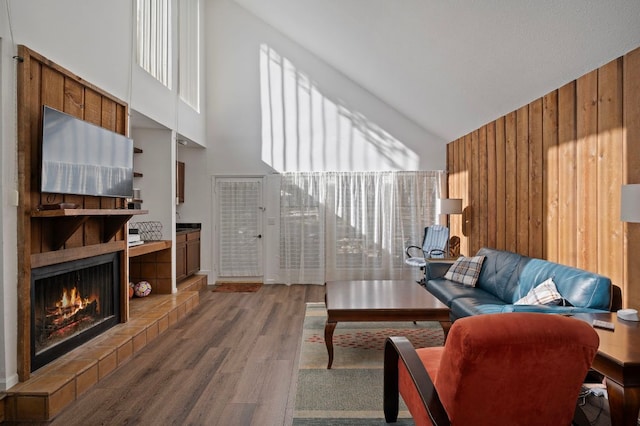 living area with wood walls, high vaulted ceiling, wood finished floors, and a tile fireplace