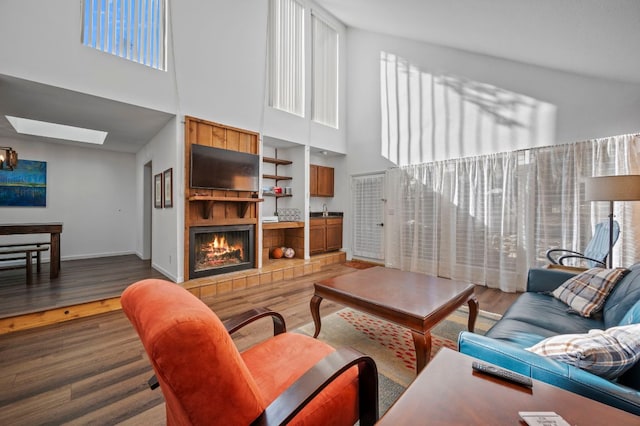 living area with a skylight, baseboards, wood finished floors, a lit fireplace, and a high ceiling