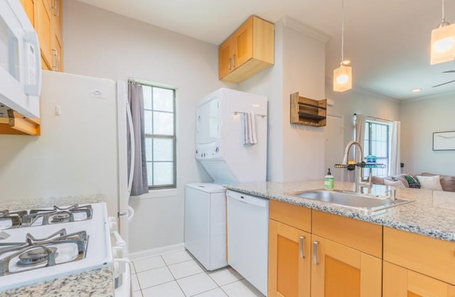 kitchen with stacked washer and dryer, hanging light fixtures, light brown cabinetry, a sink, and white appliances