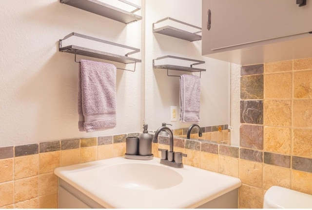 half bathroom with toilet, a wainscoted wall, vanity, and tile walls