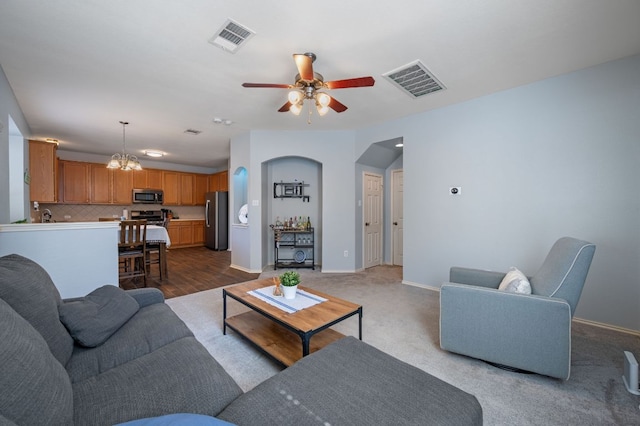 carpeted living area with visible vents, baseboards, and ceiling fan with notable chandelier