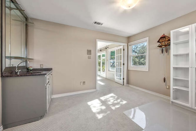 kitchen with baseboards, visible vents, a sink, and light colored carpet