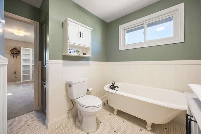 bathroom with wainscoting, a freestanding tub, toilet, and tile patterned floors