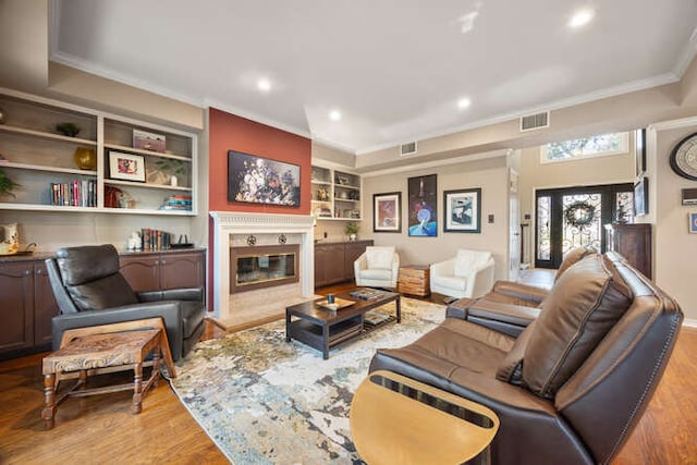 living area featuring a premium fireplace, wood finished floors, visible vents, built in features, and crown molding