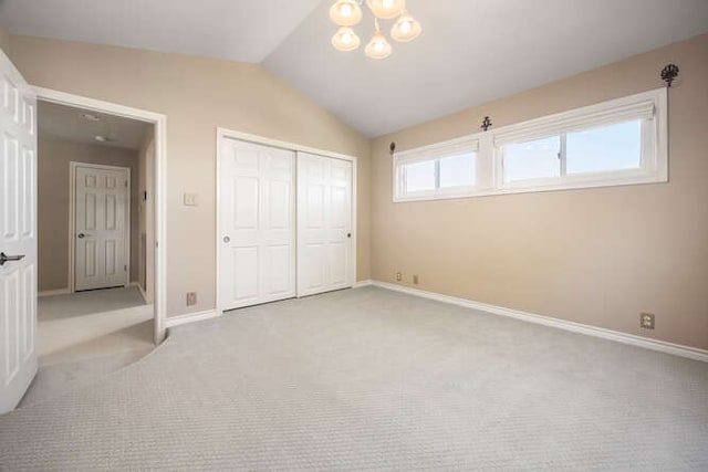 unfurnished bedroom with lofted ceiling, a closet, light colored carpet, a chandelier, and baseboards